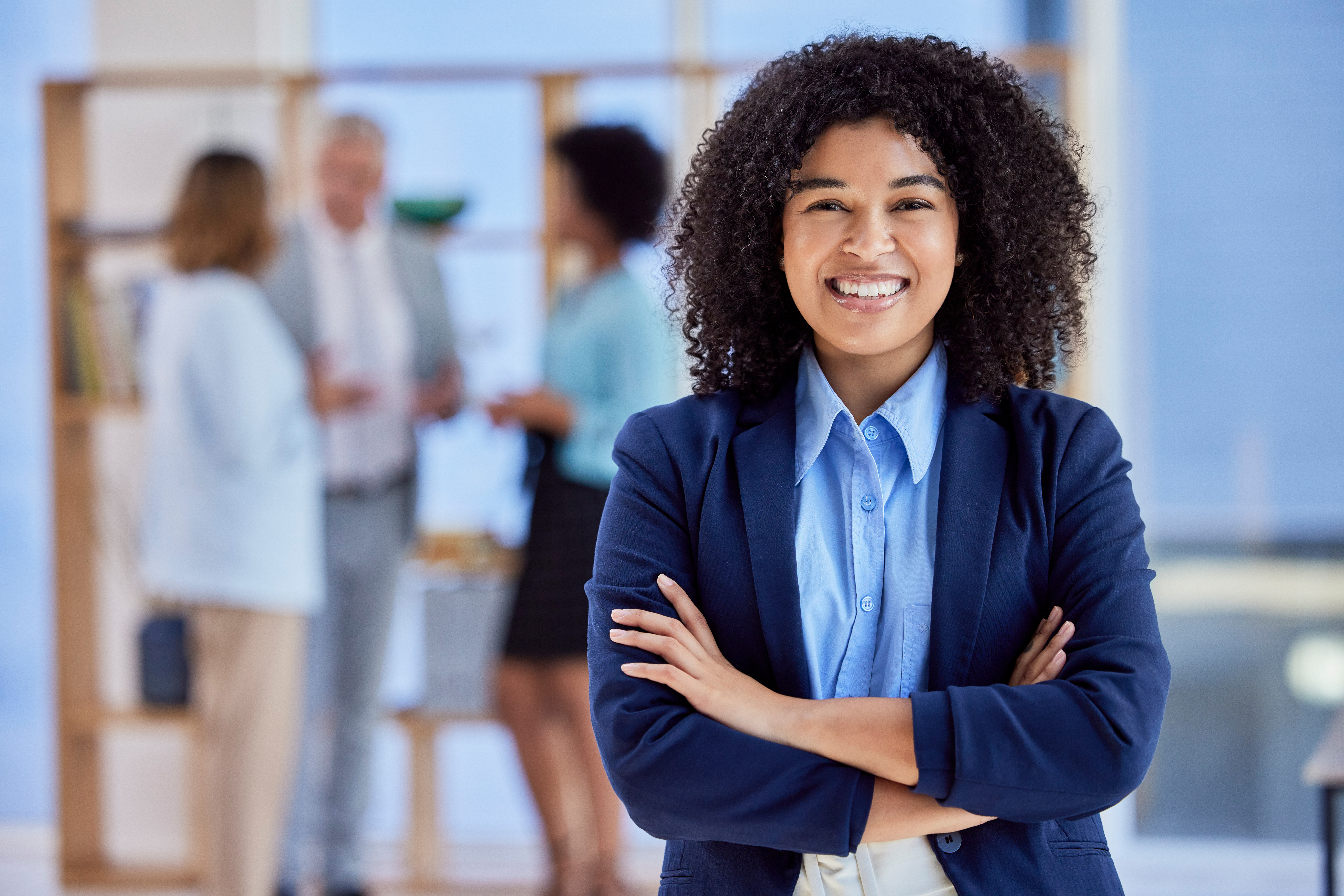 A smiling young professional in a modern office setting with her older colleagues in the background.